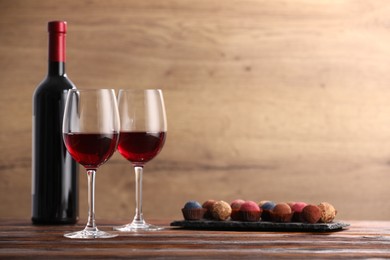 Photo of Delicious truffle bonbons and wine on wooden table. Space for text