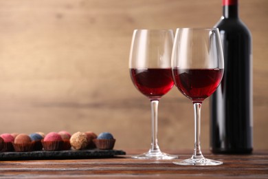 Photo of Delicious truffle bonbons and wine on wooden table. Space for text