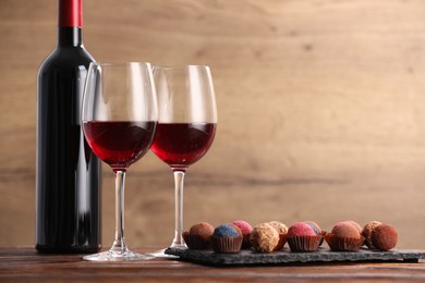 Photo of Delicious truffle bonbons and wine on wooden table. Space for text