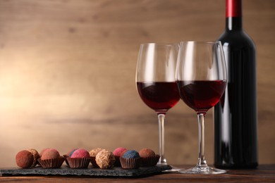 Photo of Delicious truffle bonbons and wine on wooden table. Space for text