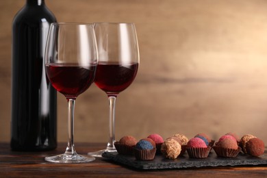 Photo of Delicious truffle bonbons and wine on wooden table. Space for text
