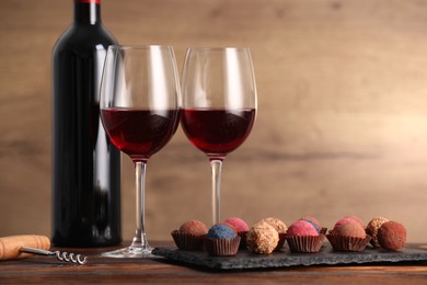 Photo of Delicious truffle bonbons and wine on wooden table. Space for text