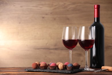 Photo of Delicious truffle bonbons and wine on wooden table. Space for text