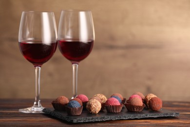 Photo of Delicious truffle bonbons and wine on wooden table. Space for text