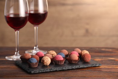 Photo of Delicious truffle bonbons and wine on wooden table. Space for text