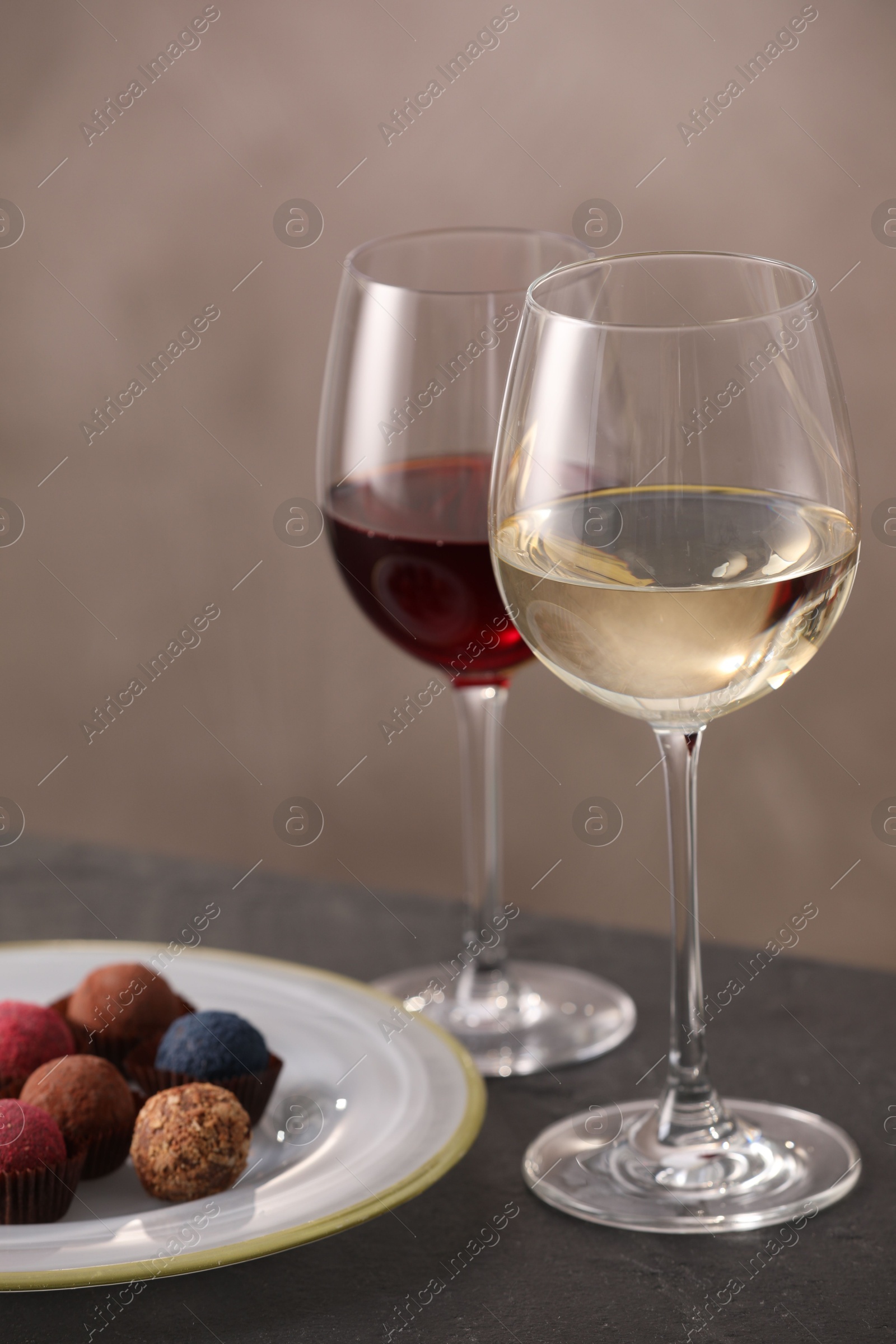 Delicious truffle bonbons and wine on black table against grey background Photo of Delicious truffle bonbons and wine on black table against grey background