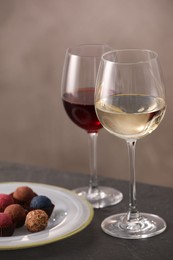 Photo of Delicious truffle bonbons and wine on black table against grey background