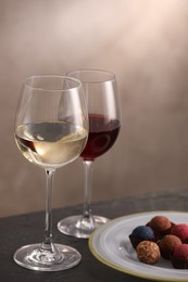 Photo of Delicious truffle bonbons and wine on black table against grey background