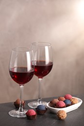 Photo of Delicious truffle bonbons and wine on black table against grey background