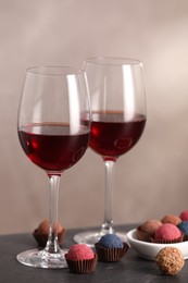 Photo of Delicious truffle bonbons and wine on black table against grey background