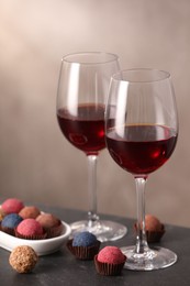 Photo of Delicious truffle bonbons and wine on black table against grey background
