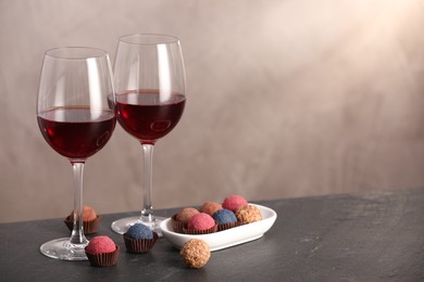 Photo of Delicious truffle bonbons and wine on black table against grey background. Space for text