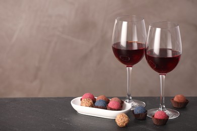Photo of Delicious truffle bonbons and wine on black table against grey background. Space for text
