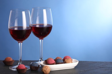 Photo of Delicious truffle bonbons and wine on black table against blue background. Space for text
