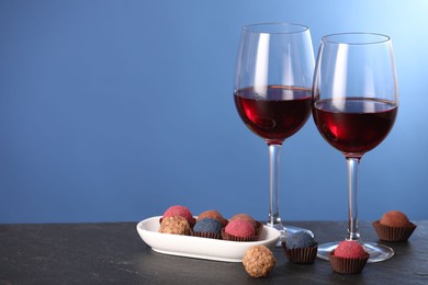 Photo of Delicious truffle bonbons and wine on black table against blue background. Space for text