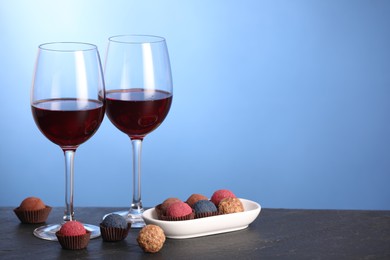 Photo of Delicious truffle bonbons and wine on black table against blue background. Space for text