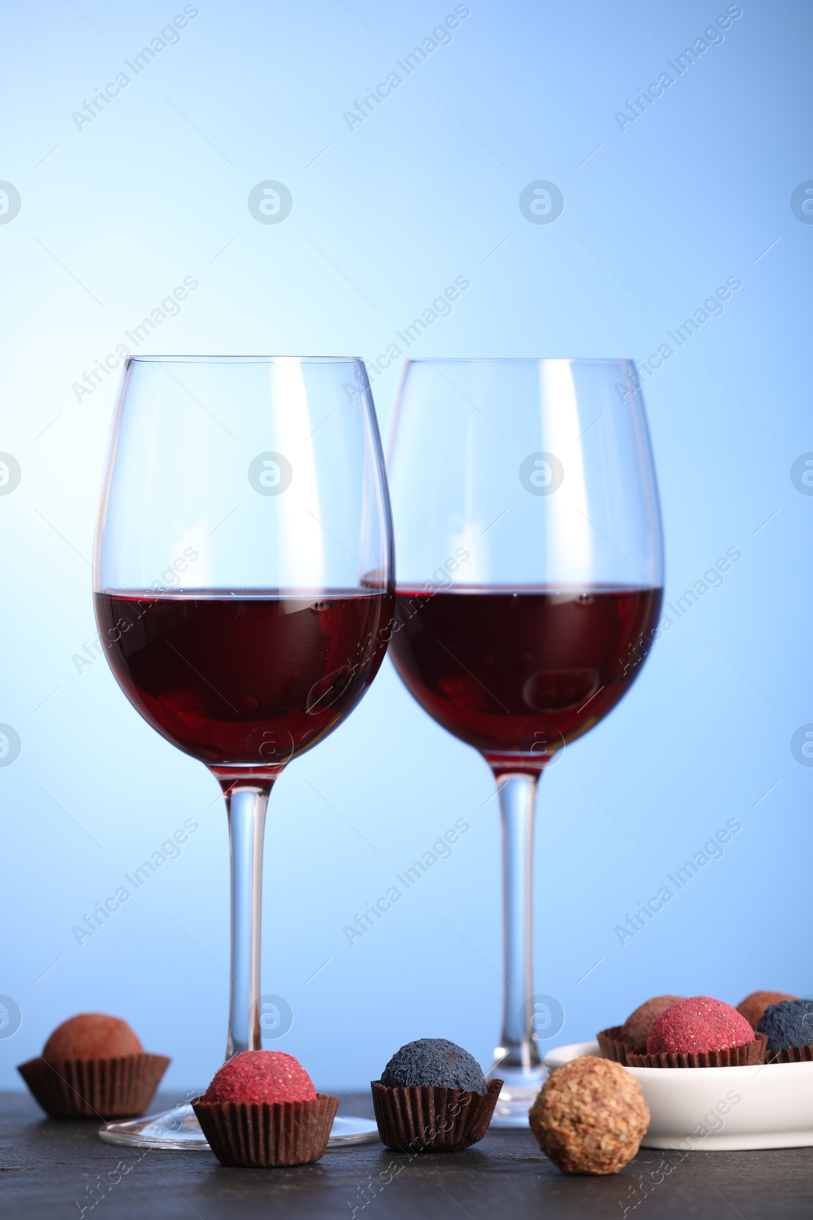 Delicious truffle bonbons and wine on black table against blue background Photo of Delicious truffle bonbons and wine on black table against blue background
