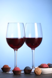 Photo of Delicious truffle bonbons and wine on black table against blue background