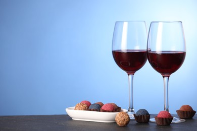 Photo of Delicious truffle bonbons and wine on black table against blue background. Space for text