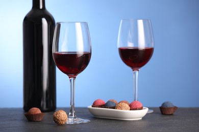 Photo of Delicious truffle bonbons and wine on black table against blue background