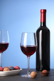 Photo of Delicious truffle bonbons and wine on black table against blue background