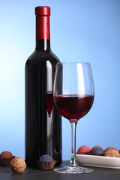 Photo of Delicious truffle bonbons and wine on black table against blue background