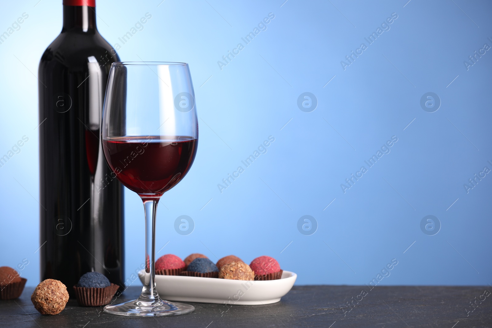 Delicious truffle bonbons and wine on black table against blue background. Space for text Photo of Delicious truffle bonbons and wine on black table against blue background. Space for text