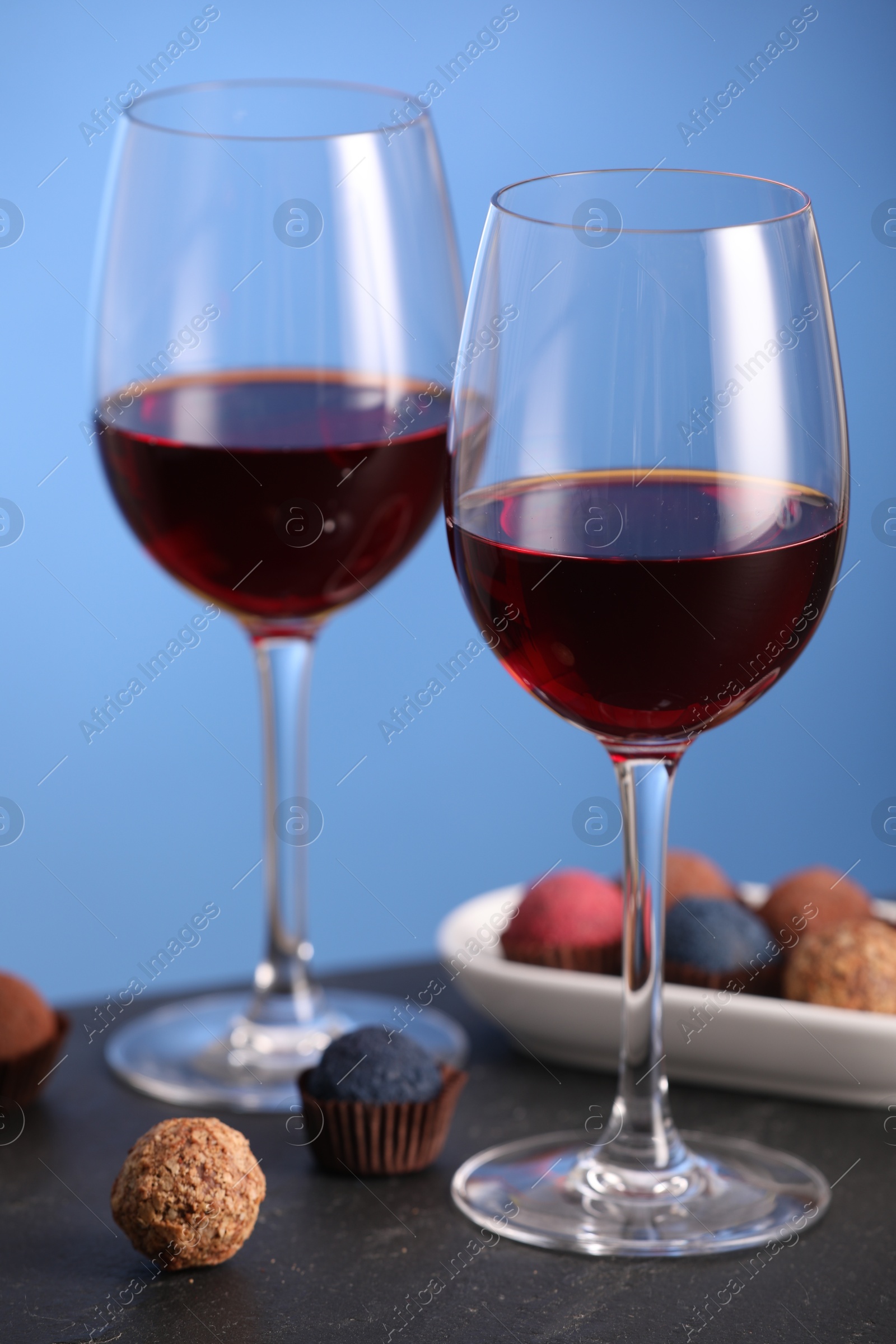 Delicious truffle bonbons and wine on black table against blue background Photo of Delicious truffle bonbons and wine on black table against blue background
