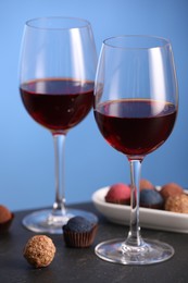 Photo of Delicious truffle bonbons and wine on black table against blue background