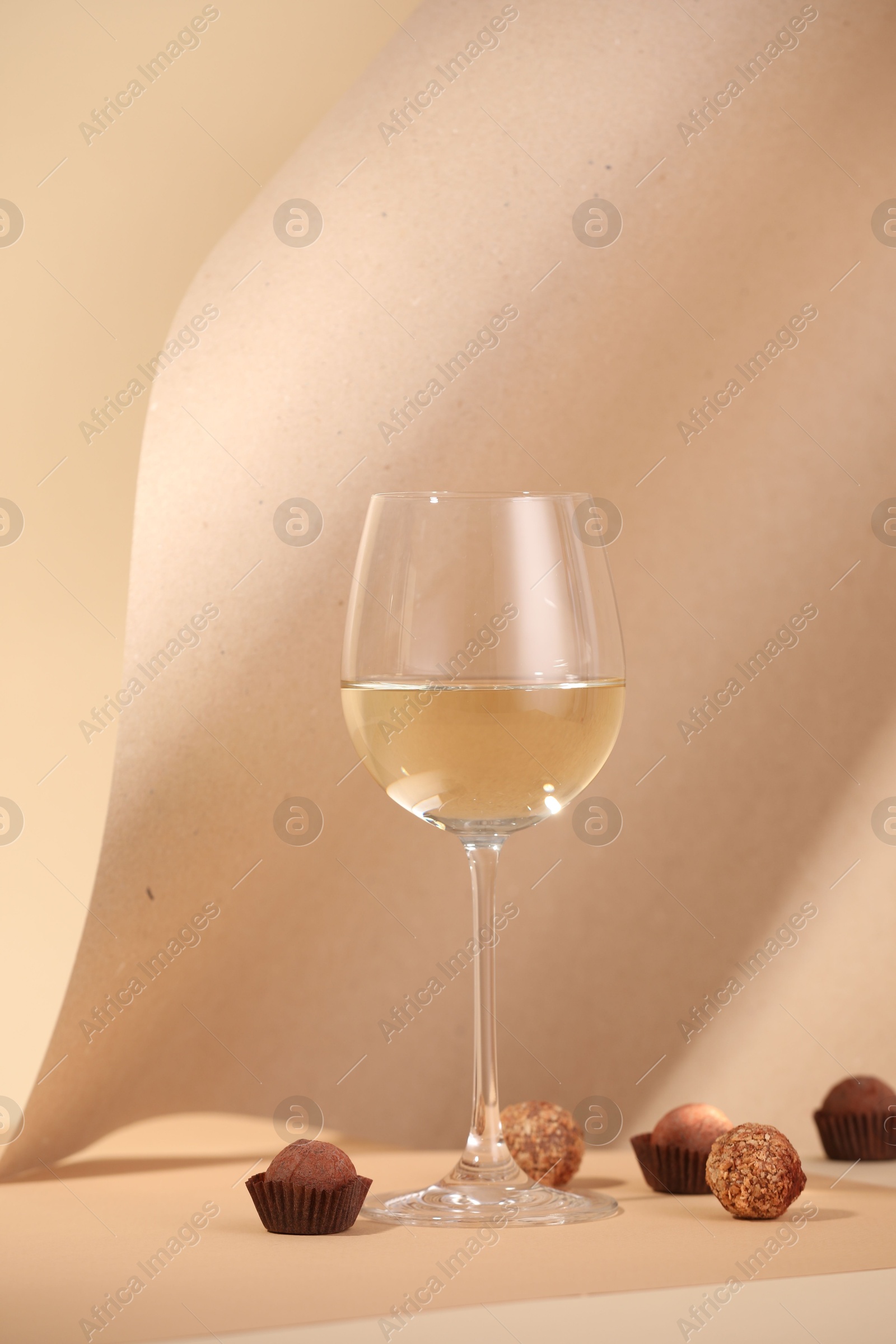 Delicious truffle bonbons and wine on beige background Photo of Delicious truffle bonbons and wine on beige background