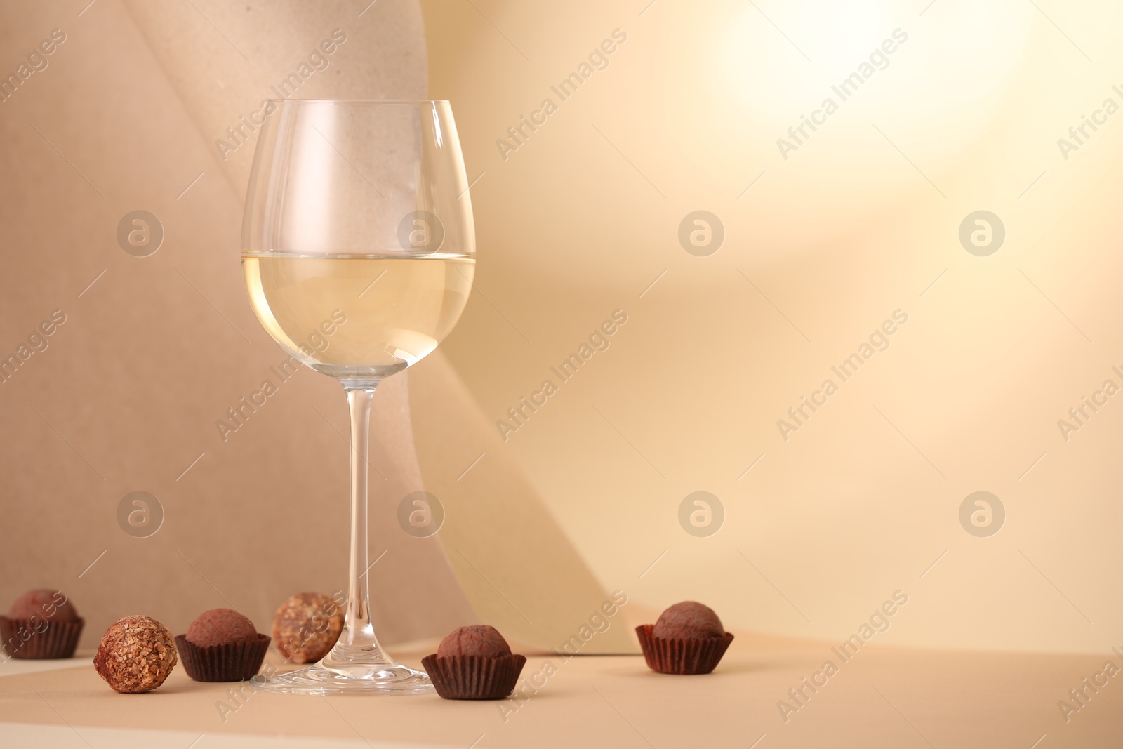 Delicious truffle bonbons and wine on beige background. Space for text Photo of Delicious truffle bonbons and wine on beige background. Space for text