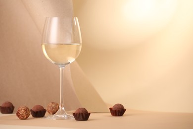 Photo of Delicious truffle bonbons and wine on beige background. Space for text