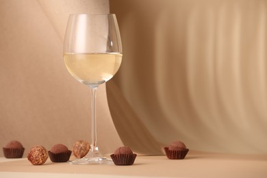 Photo of Delicious truffle bonbons and wine on beige background. Space for text