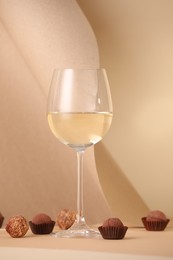 Photo of Delicious truffle bonbons and wine on beige background
