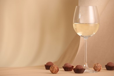 Photo of Delicious truffle bonbons and wine on beige background. Space for text