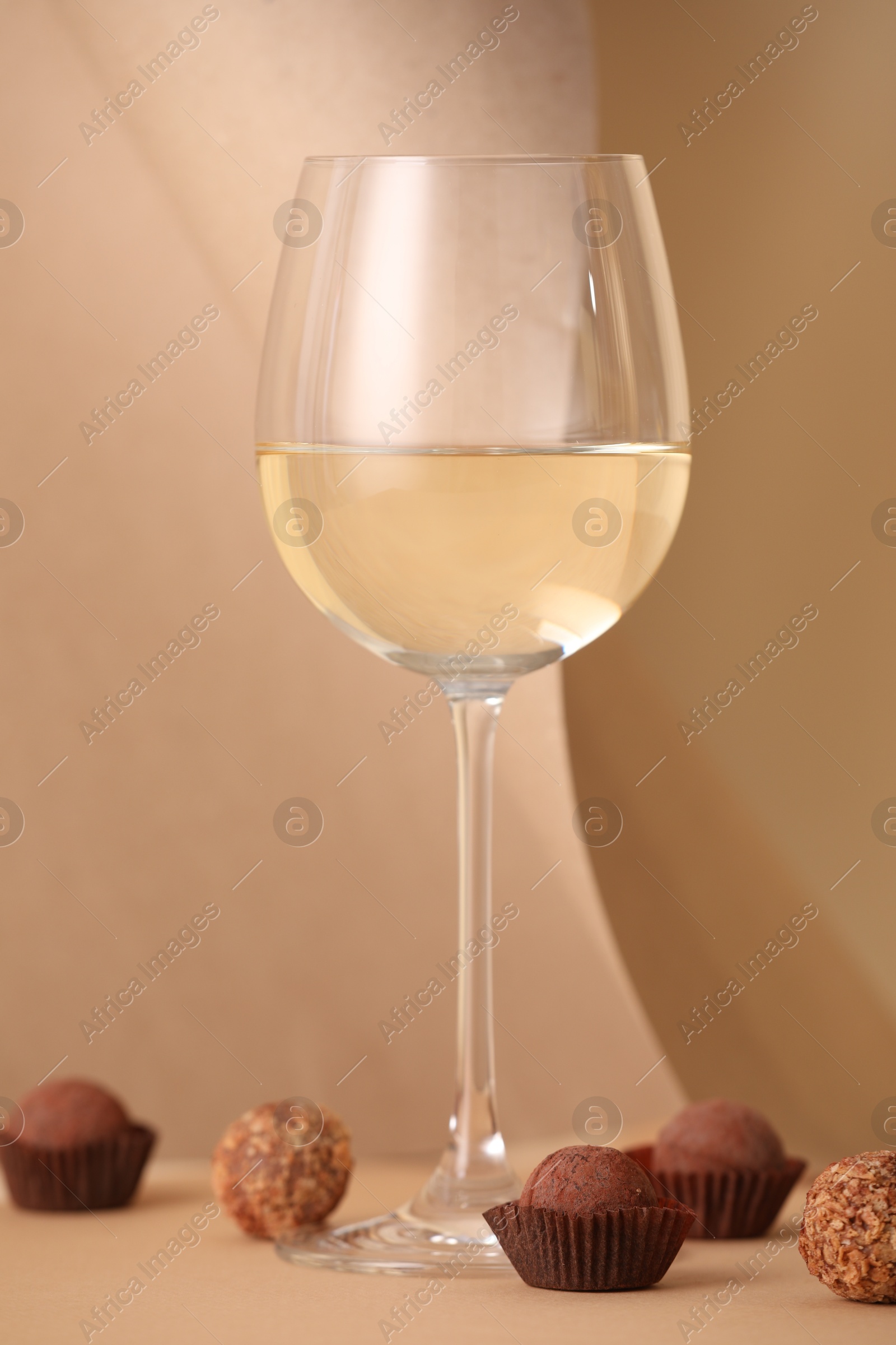 Delicious truffle bonbons and wine on beige background Photo of Delicious truffle bonbons and wine on beige background