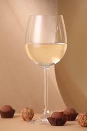 Photo of Delicious truffle bonbons and wine on beige background