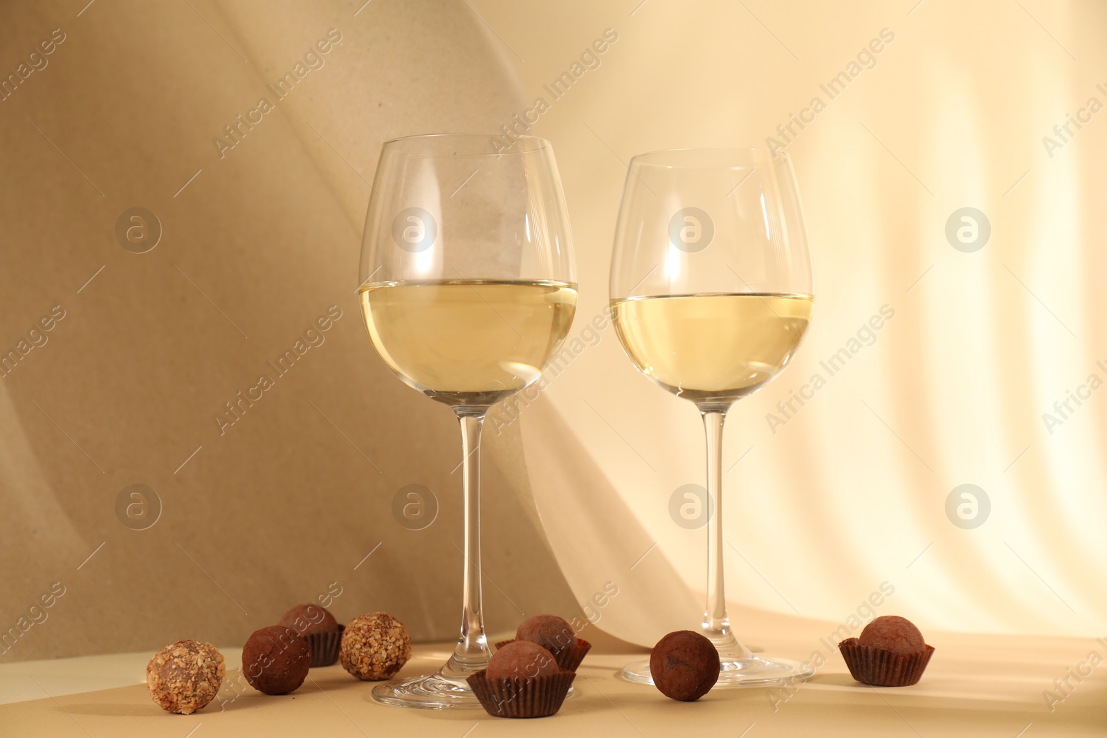 Photo of Delicious truffle bonbons and wine on beige background