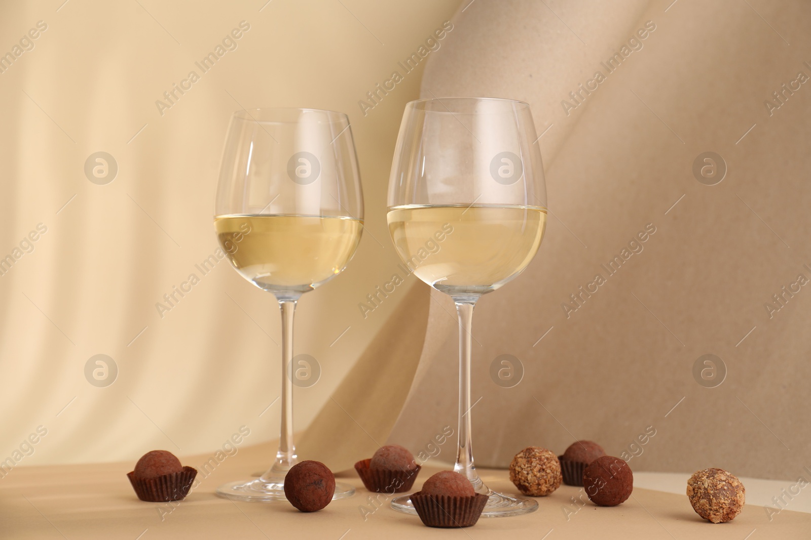 Delicious truffle bonbons and wine on beige background Photo of Delicious truffle bonbons and wine on beige background