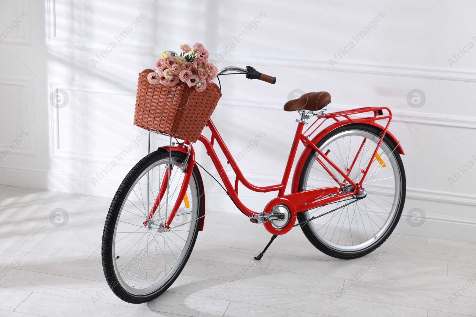 Bicycle with basket of beautiful flowers near white wall indoors Photo of Bicycle with basket of beautiful flowers near white wall indoors