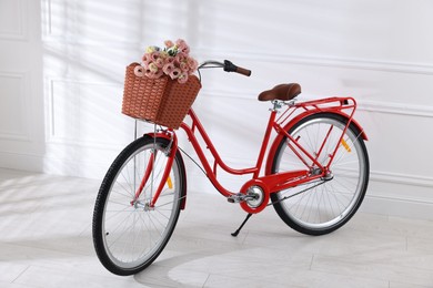 Photo of Bicycle with basket of beautiful flowers near white wall indoors