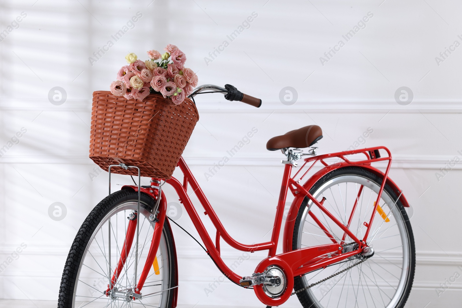 Photo of Bicycle with basket of beautiful flowers near white wall indoors