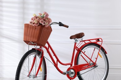 Photo of Bicycle with basket of beautiful flowers near white wall indoors