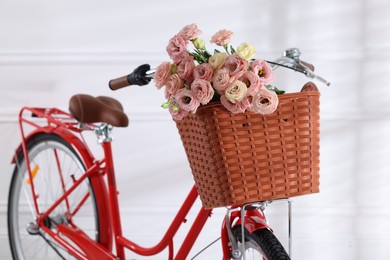 Photo of Bicycle with basket of beautiful flowers near white wall indoors, closeup