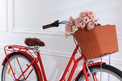Photo of Bicycle with basket of beautiful flowers near white wall indoors, closeup