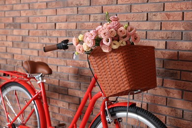 Photo of Bicycle with basket of beautiful flowers near brick wall indoors, closeup