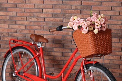 Photo of Bicycle with basket of beautiful flowers near brick wall indoors, closeup