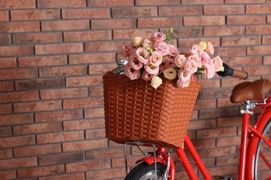 Photo of Bicycle with basket of beautiful flowers near brick wall indoors, closeup. Space for text