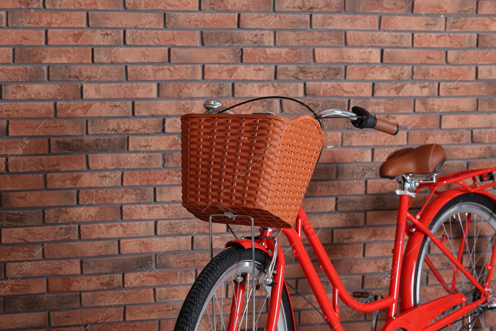 Red bicycle with basket near brick wall indoors, closeup. Space for text Photo of Red bicycle with basket near brick wall indoors, closeup. Space for text