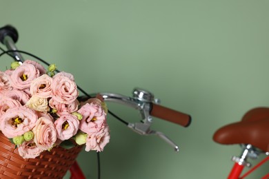 Photo of Bicycle with basket of beautiful flowers near light green wall indoors, closeup. Space for text